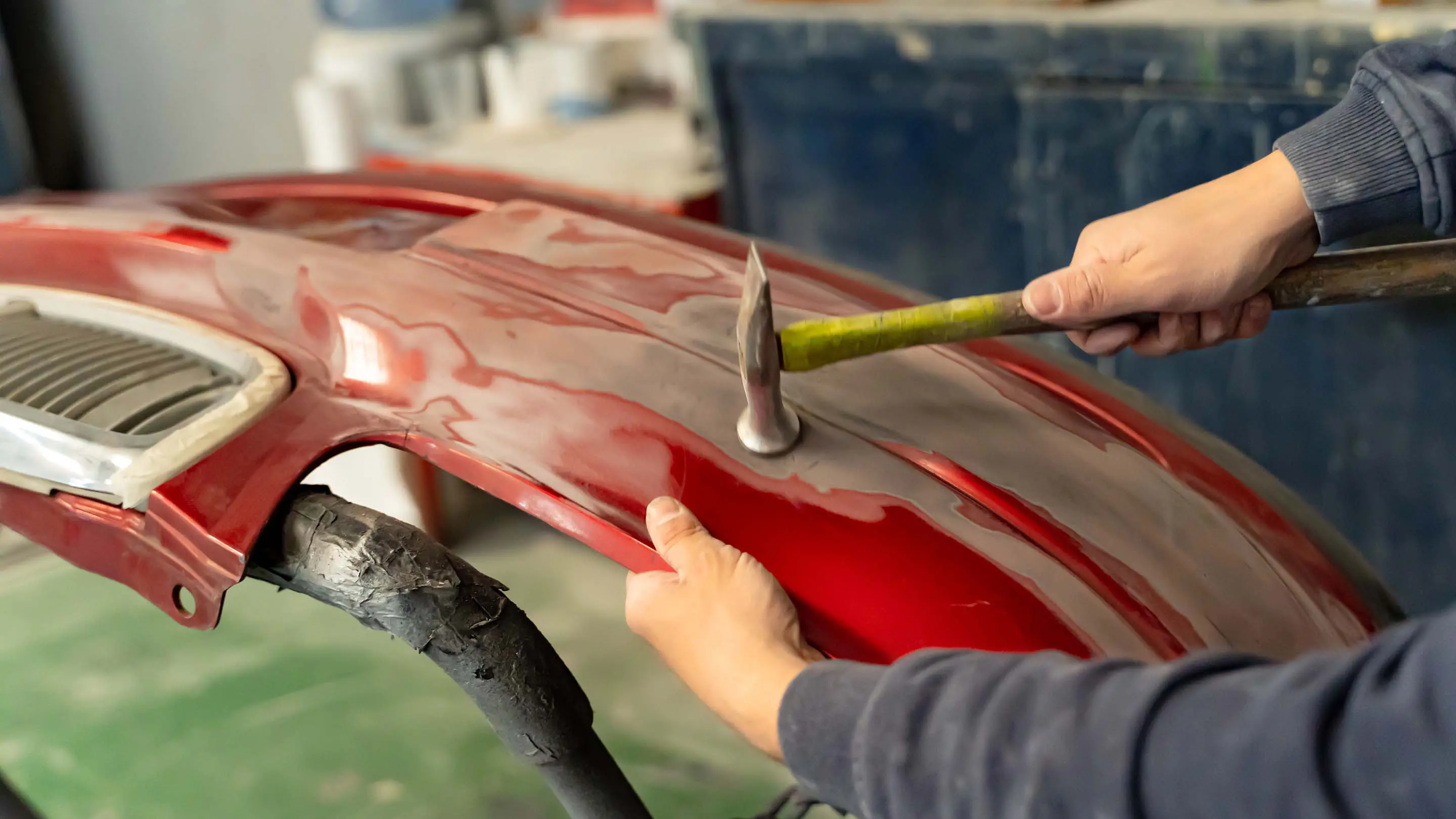 赤い車外装部品をハンマーで叩いている様子